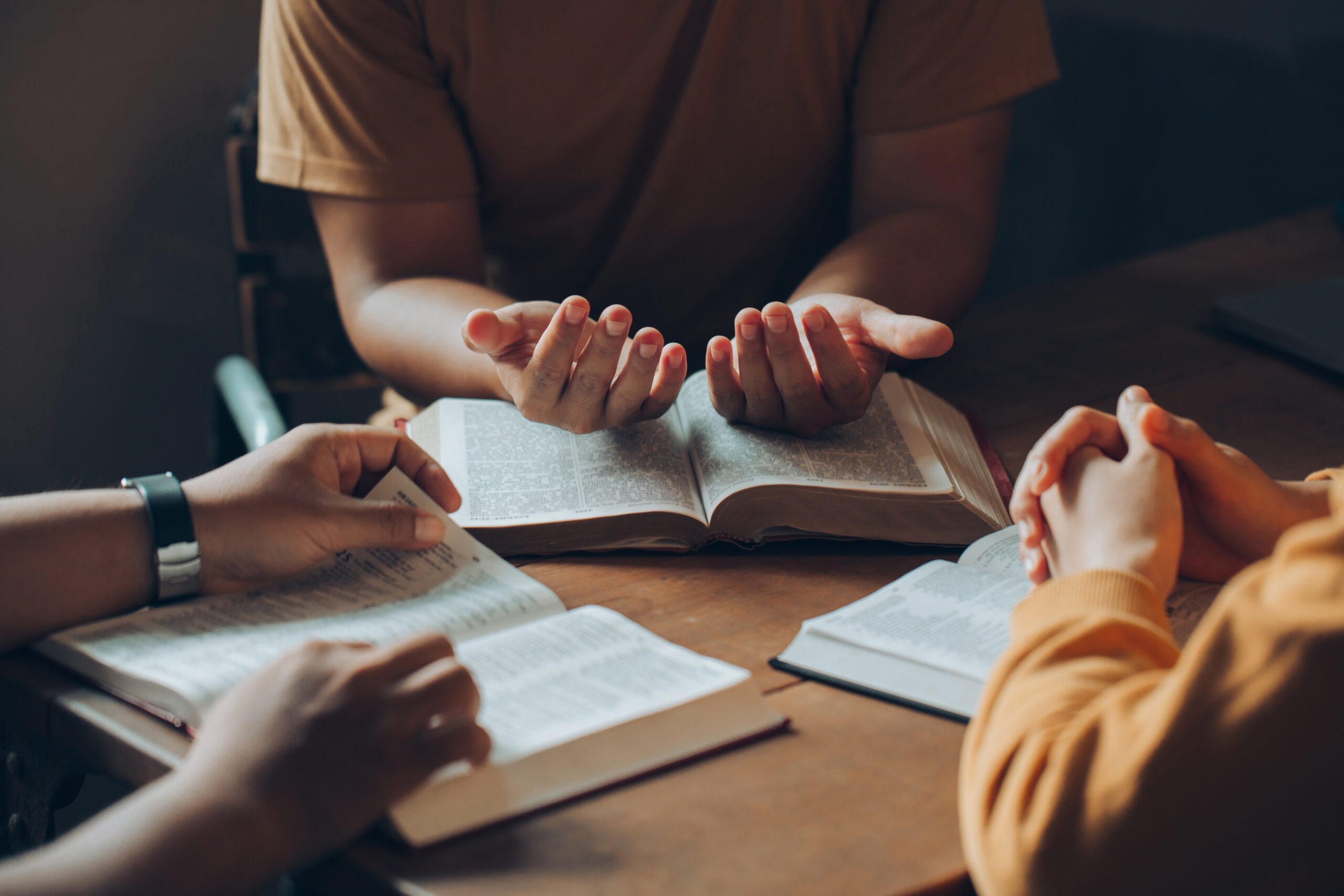 Christians and Bible study concept.Christian family sitting around a wooden table with open bible page and holding each other's hand praying together.